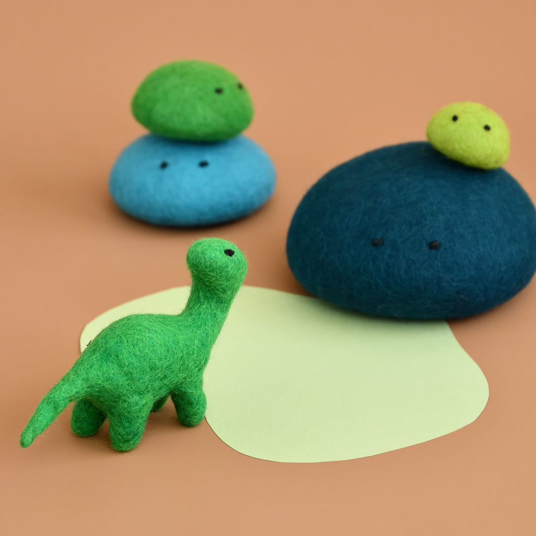 Miniature green felt brontosaurus toy standing at a waterhole